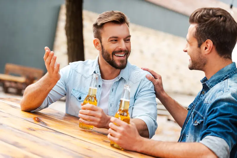 Two males sitting at a table drinking beer and talking